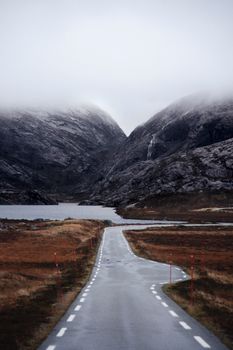 Foggy road leads to misty mountain peaks, offering a serene travel scene.