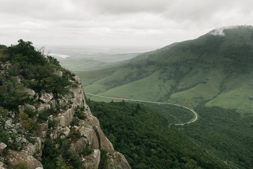 Free A breathtaking aerial view of lush green hills and valleys, featuring a winding road under a cloudy sky. Stock Photo