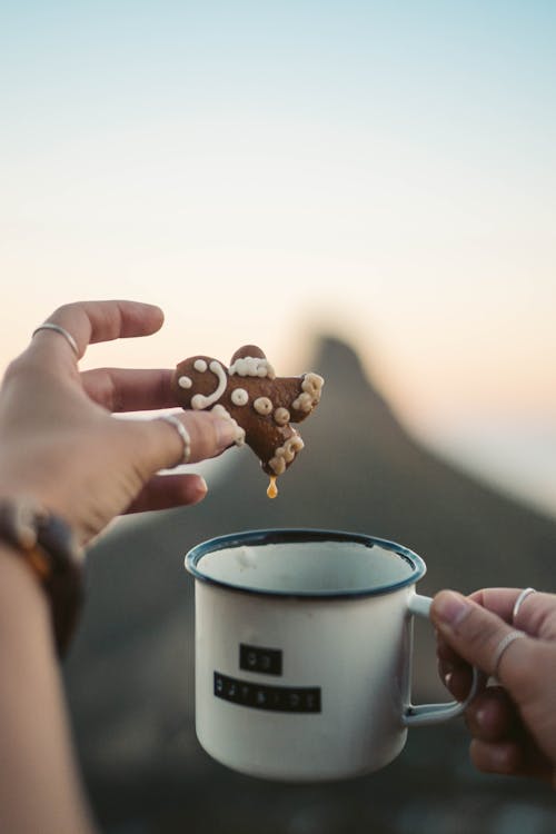 A Person Holding a Cup of Coffee and a Gingerbread Cookie