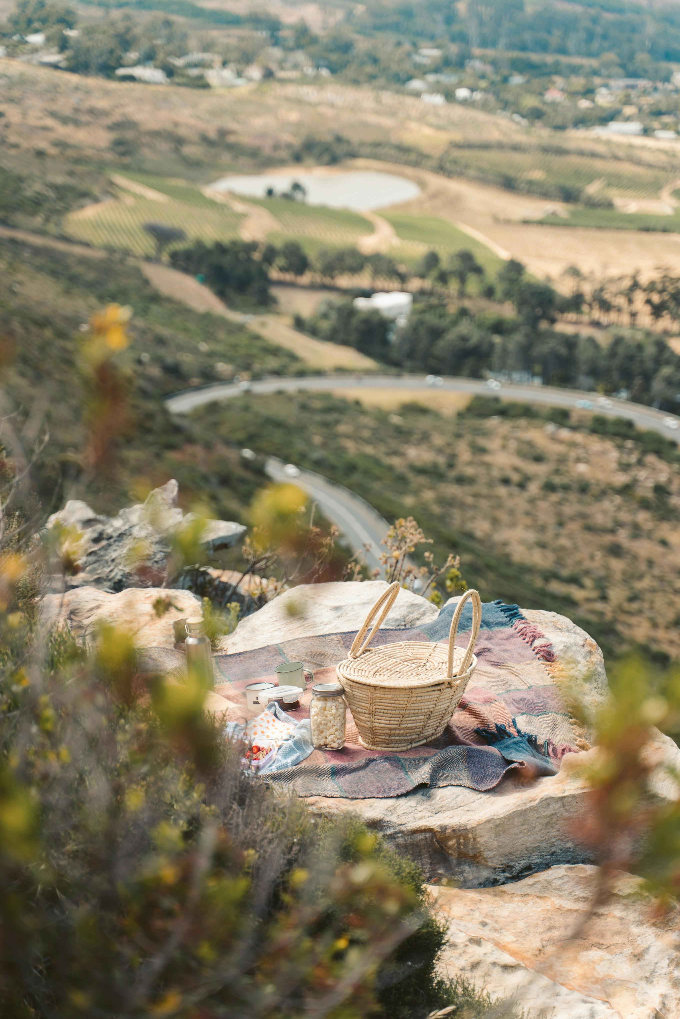 Enjoy a serene picnic atop a hill with breathtaking views of a lush valley and winding roads below.