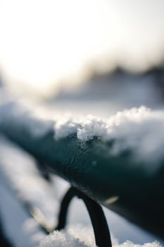 Detailed view of snowy metal railing with blurred background, showcasing winter scenery.