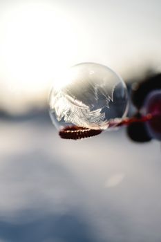 Close-up of a frozen soap bubble in the winter sunlight, creating a magical ice crystal effect.