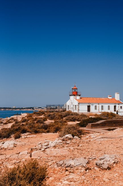 A picturesque view of a lighthouse on the rocky Algarve coastline under a bright blue sky.