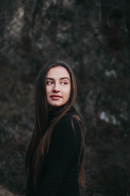 Free Outdoor portrait of a woman with long hair, looking back, wearing black clothing. Stock Photo