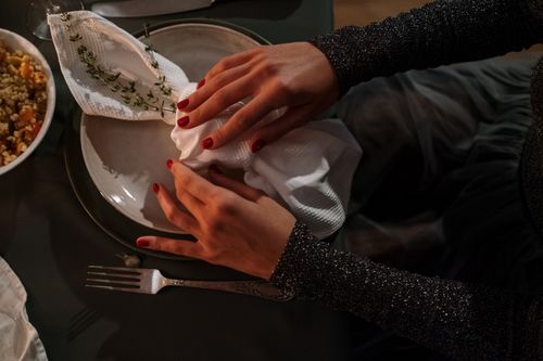 Free Close-up of hands elegantly arranging a napkin on a plate, capturing a moody dining atmosphere. Stock Photo