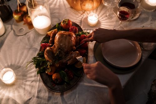 Free A warm holiday dinner setting featuring a roast turkey being sliced on a candlelit table. Stock Photo