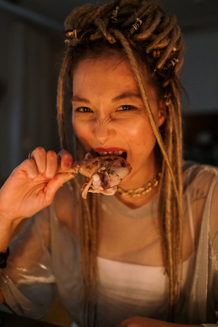 A Young Woman With Dreadlocks Eating Leg Part Of Chicken