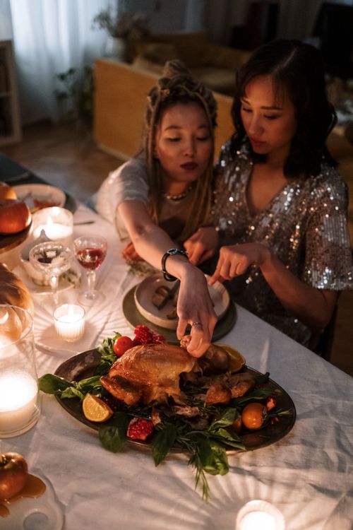 Free Two women enjoying a cozy candlelit dinner with a roast centerpiece in a stylish living room. Stock Photo