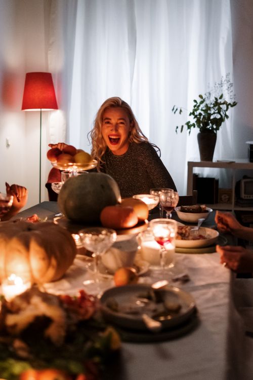 Free Blonde woman enjoying festive holiday dinner with friends around a candlelit table. Stock Photo