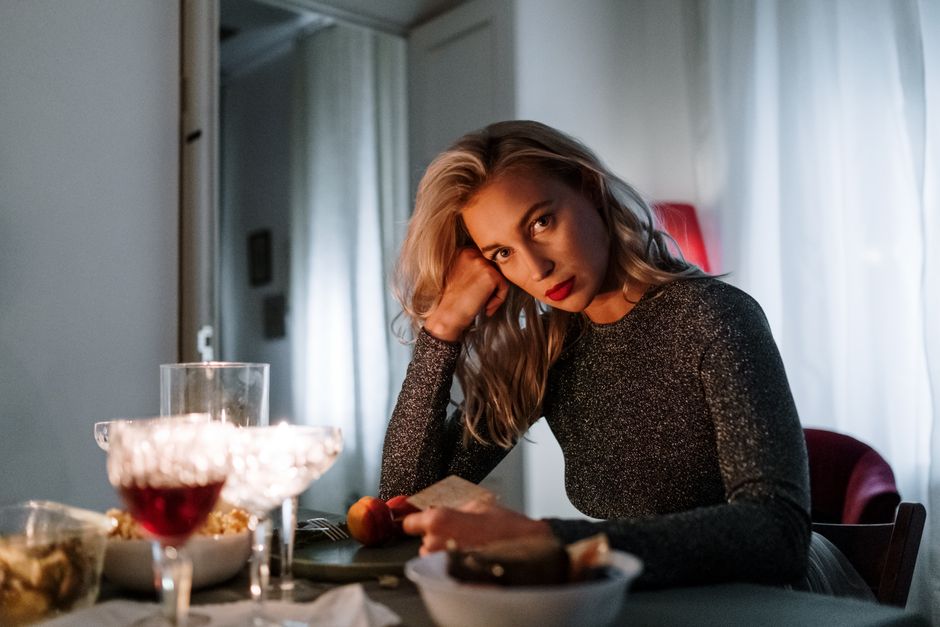 Caucasian woman with red lips posing at a dimly lit dinner table indoors.