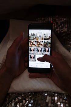 Hands holding a smartphone while scrolling through photos in a dimly lit setting.