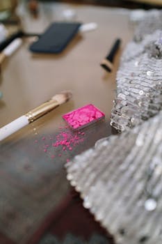 Close-up of a broken pink eyeshadow with a makeup brush on a sequin surface, artistic still life.