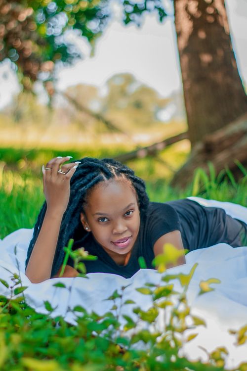 Free Content young African American female in casual outfit with dreadlocks lying on plaid leaning on hand in park and looking at camera Stock Photo
