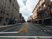 Straight asphalt roadway with marking lines between aged multistory building exteriors under cloudy sky in town