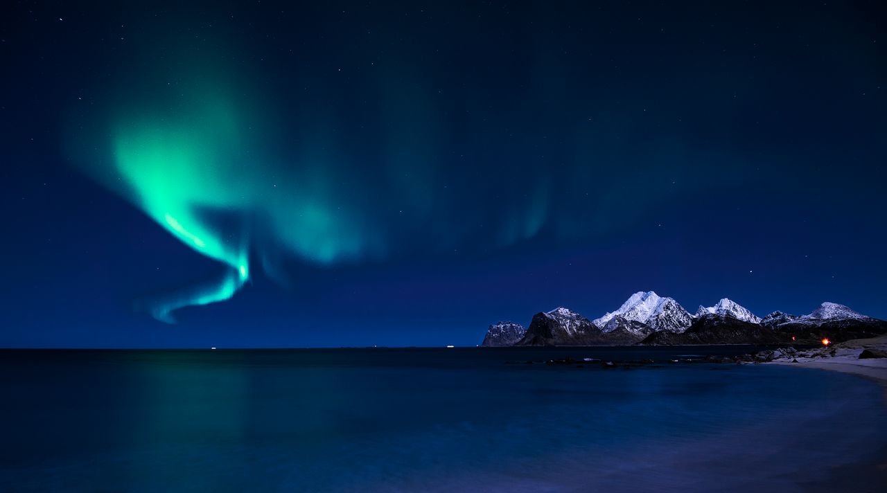 stunning aurora borealis over snowy mountain range with sea view