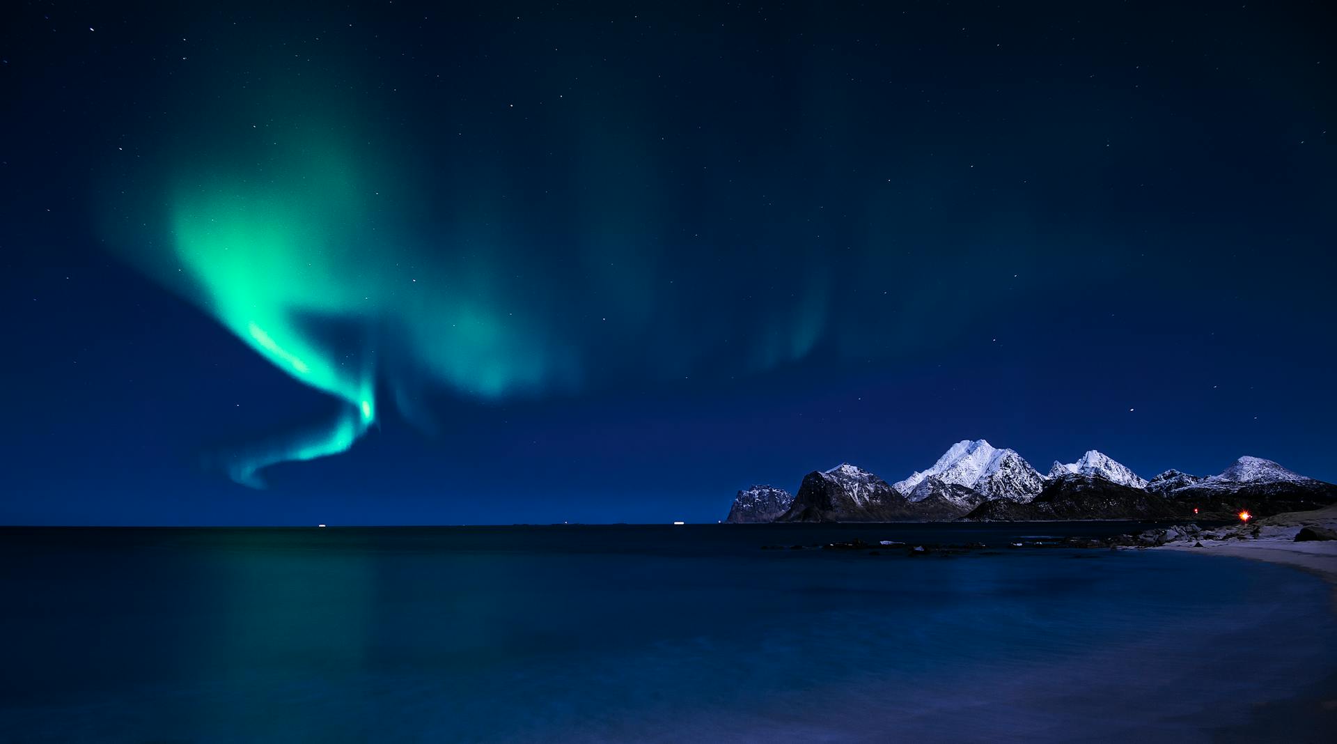 Stunning aurora borealis over snowy mountain range with sea view.