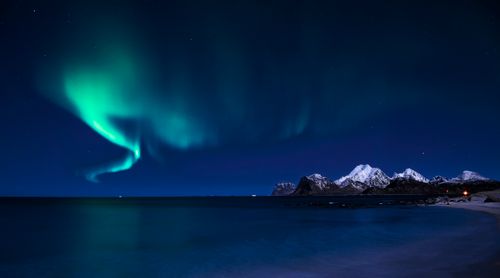 Free Stunning aurora borealis over snowy mountain range with sea view. Stock Photo