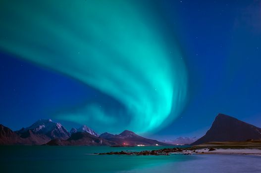 A breathtaking display of the aurora borealis over snow-capped mountains and calm sea at night.