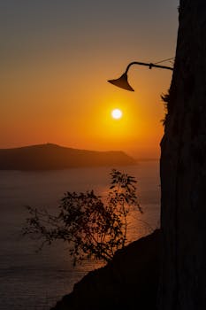 Breathtaking Santorini sunset with a silhouetted lamp and vibrant golden hues over the Aegean Sea.