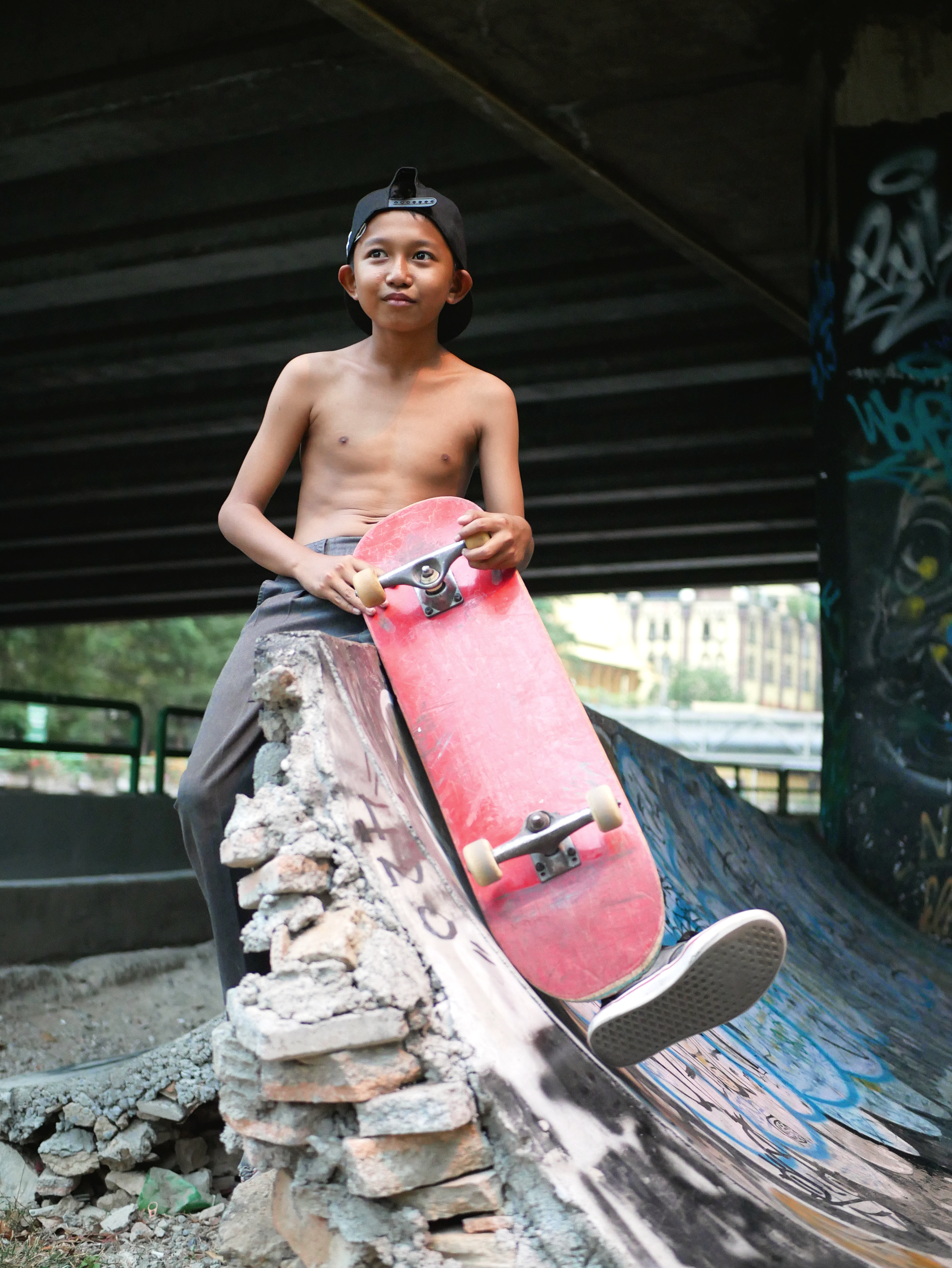 Teenager posing with a skateboard under an urban bridge. Bold and adventurous.
