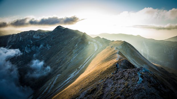 A breathtaking view of the Sibillini Mountains at sunrise with golden sunlight casting over the peaks.