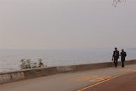 两名西装男子沿着海边步道在朦胧的天空下漫步