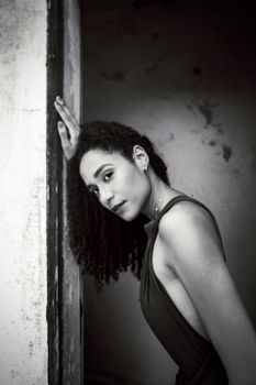 Black and white portrait of a woman in a sleeveless dress leaning against a textured wall.