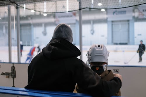 A Man and a Boy Watching People Playing Ice Hockey