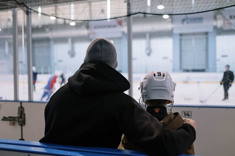 A Man And A Boy Watching People Playing Ice Hockey