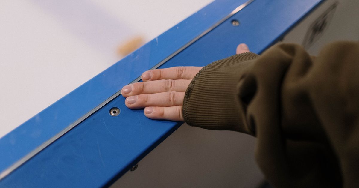A hand in a green sleeve touching a blue ice rink barrier, emphasizing texture and detail.