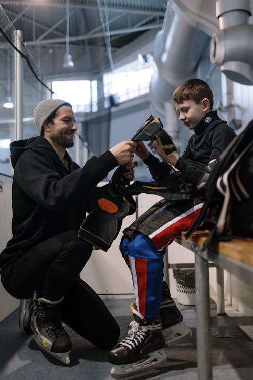Free A Man Helping a Boy Wear Ice Hockey Sports Gear Stock Photo