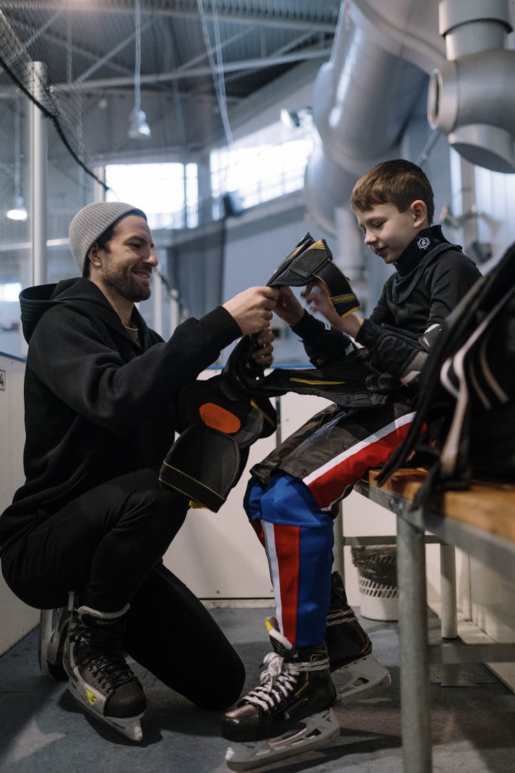 A Man Helping A Boy Wear Ice Hockey Sports Gear