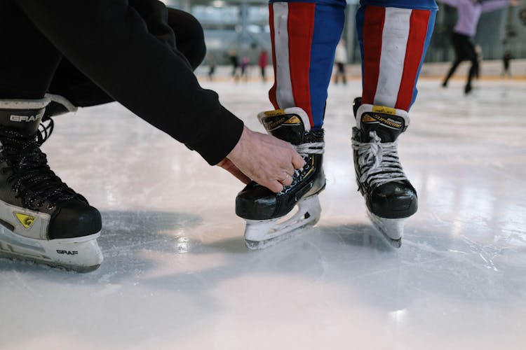 A Person Tying The Shoelaces Of A Child's Ice Skates