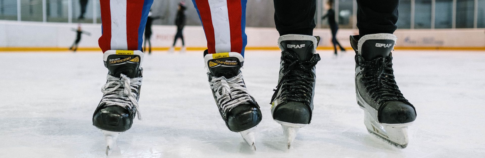 Close-up of two people in ice skates standing on an indoor ice rink.