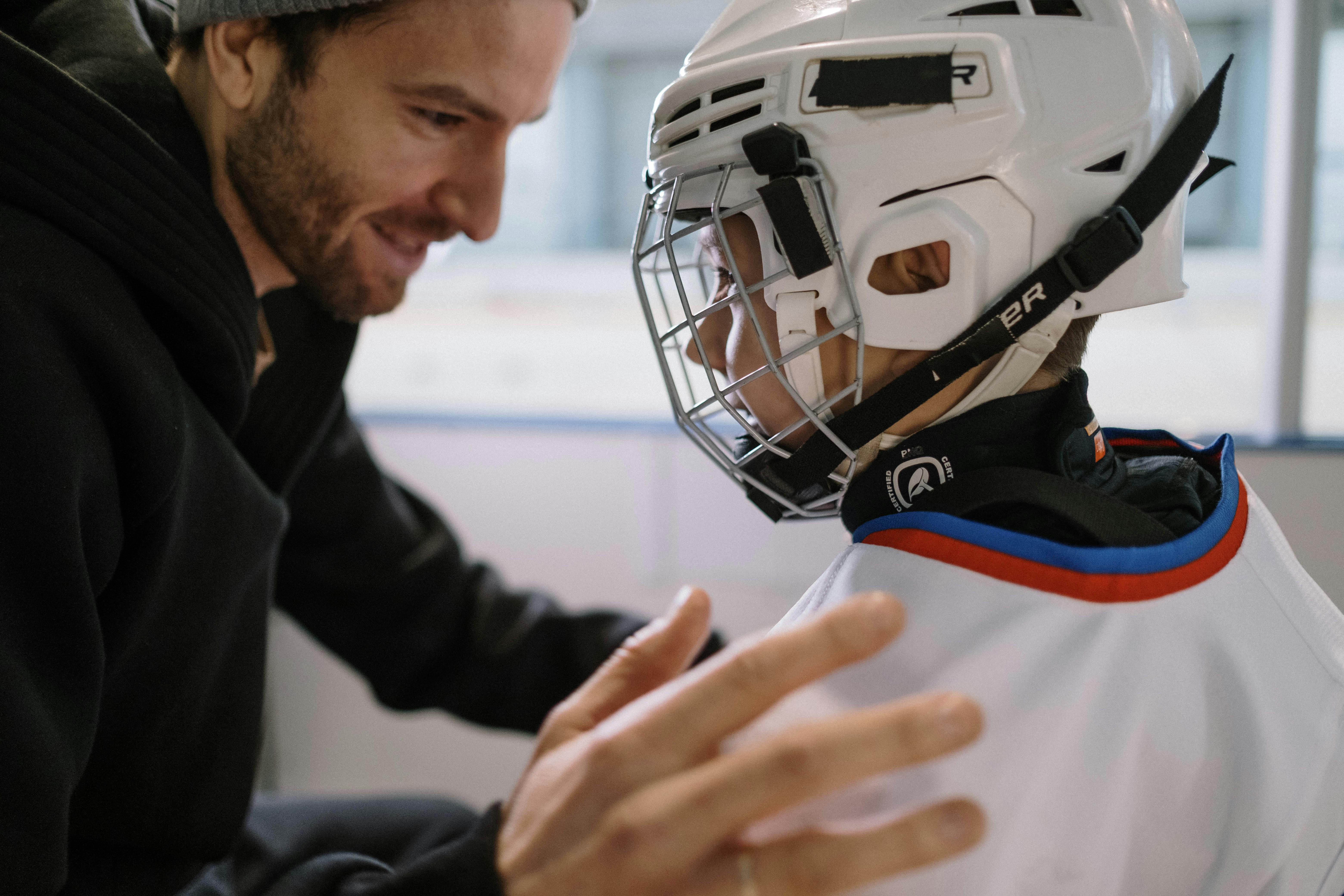 father cheering up little boy in ice hockey jersey and helmet