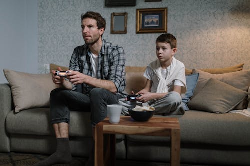 A Man and a Kid Playing Video Games while Sitting on the Sofa