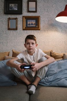 A boy intensely focused on playing video games while sitting on a couch indoors.