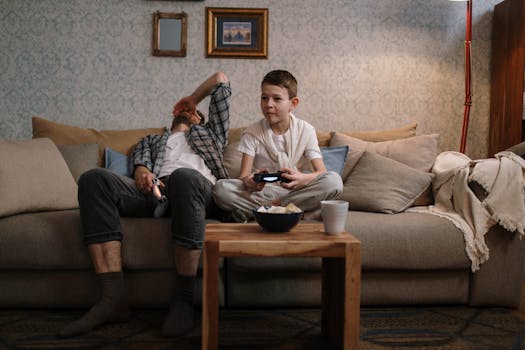 Father and son relaxing and playing video games on a cozy living room sofa.