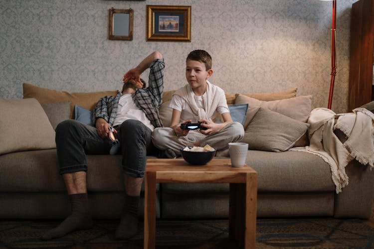 A Man And A Kid Playing Video Games While Sitting On The Sofa