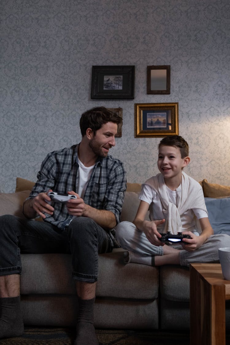 A Man And A Kid Playing Video Games While Sitting On The Sofa