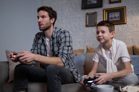A father and son bonding over video games on a cozy couch at home.