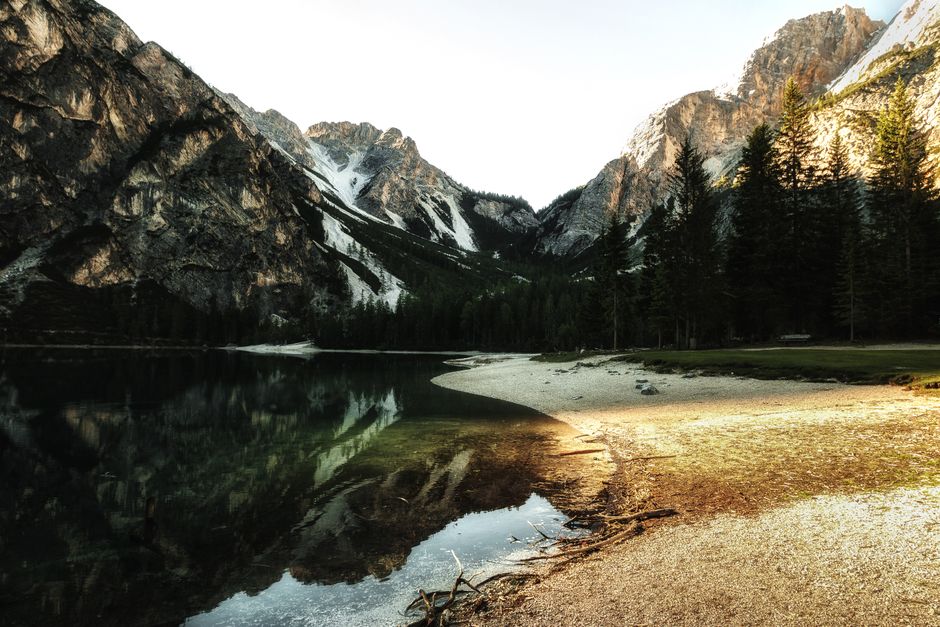 Serene mountain lake with reflection of peaks and trees at sunrise.