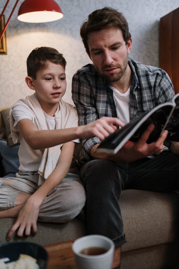 Photo Of Man And A Boy Reading Magazine Together