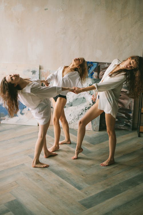 Ladies in shirts dancing near paintings in studio