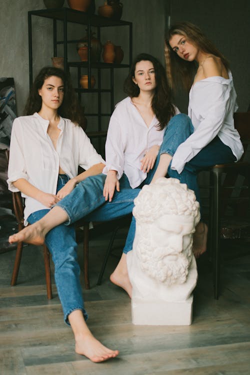 Alluring young women in similar outfits resting in art studio