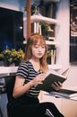 Young clever serious ethnic student with red hair in striped T shirt reading book