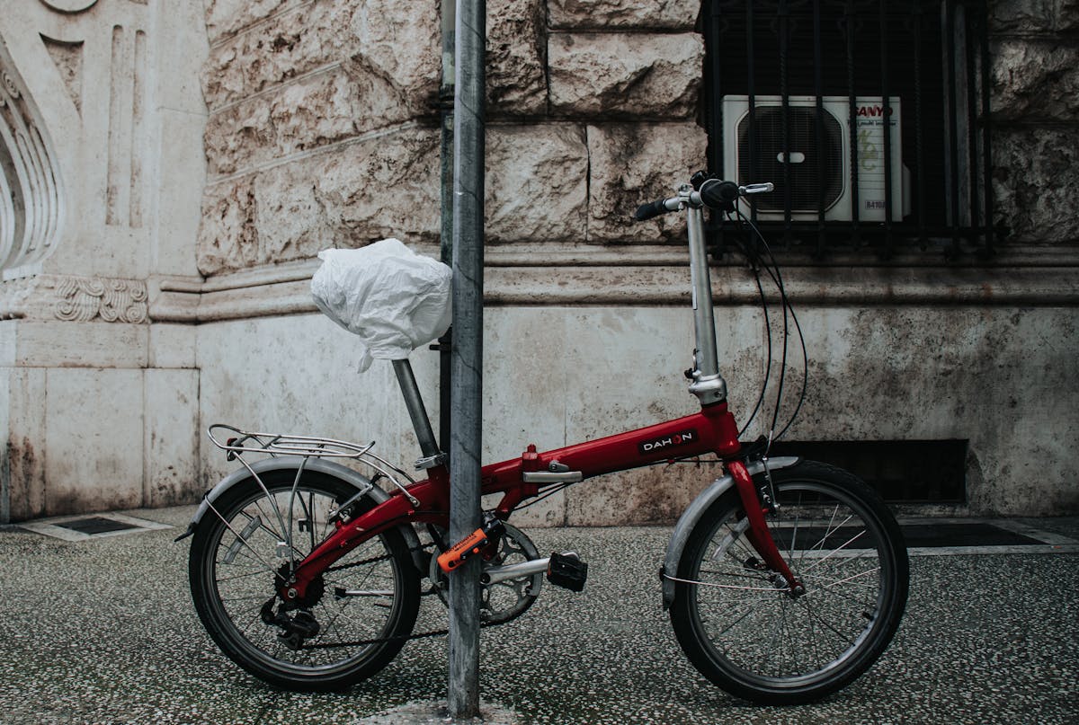 Bicicletta pieghevole rossa incatenata a un palo su marciapiede urbano