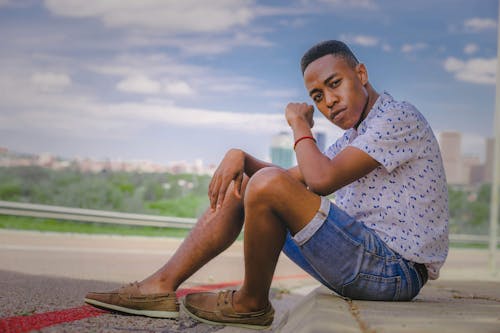 A Man in Floral Shirt and Denim Shorts Sitting on the Street