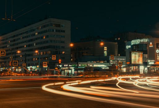 City district with asphalt road with orange lights near modern buildings under dark sky at night