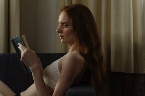 Free Woman with long hair relaxing indoors, reading a book in soft lighting. Stock Photo
